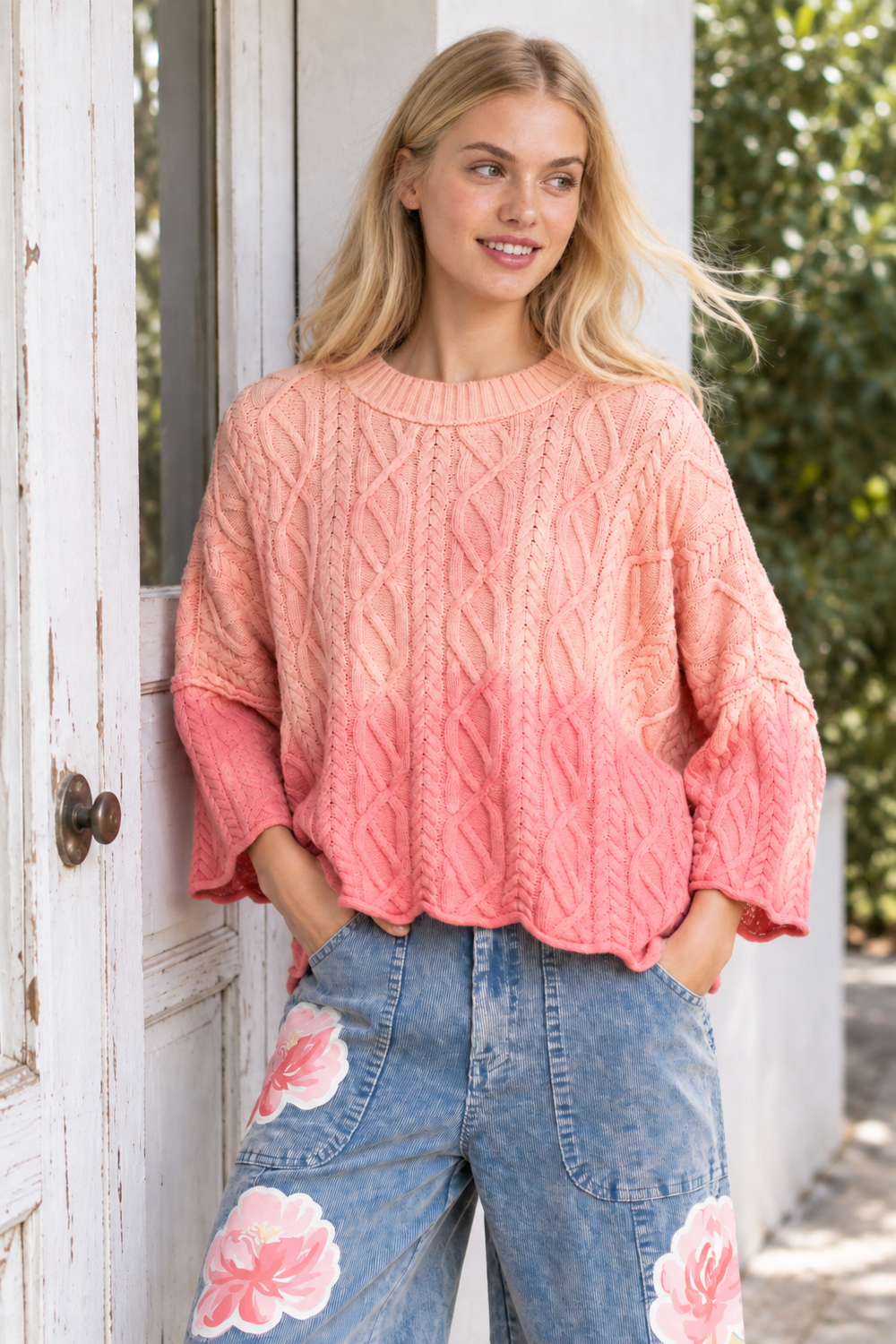 Evara pink ombre cable-knit sweater styled on a model beside a white doorway.